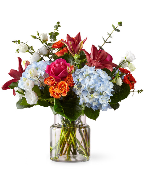 Pink, orange, blue and white flowers arranged in a cinched glass vase