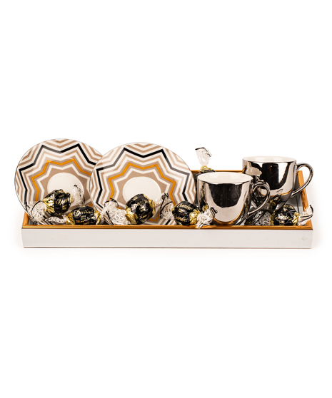 Espresso gift tray with two silver cups, geometric saucers, chocolates, and white-and-gold presentation tray