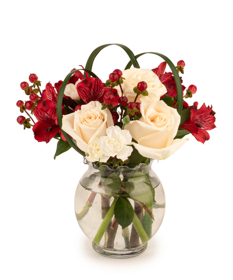 Flower arrangement with white roses, red alstroemeria, mini carnations, hypericum berries, and lily grass in a clear vase.