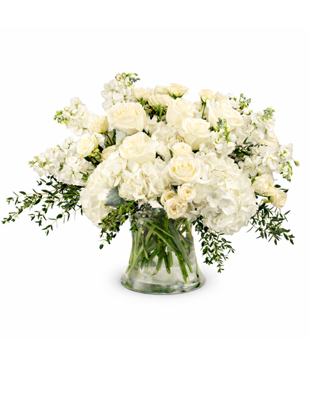 White sympathy flower arrangement with roses, hydrangeas, and soft greenery in a clear glass vase