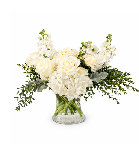 White sympathy flower arrangement with roses, hydrangeas, and soft greenery in a clear glass vase