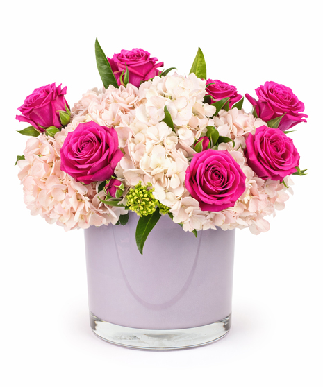 Pink roses and blush hydrangea arranged in a blush glass vase with greenery