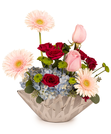 Blushing Harmony Bouquet with pink gerberas, pink roses, hot pink spray roses, blue hydrangea, and green kermit mums in a glass vase.