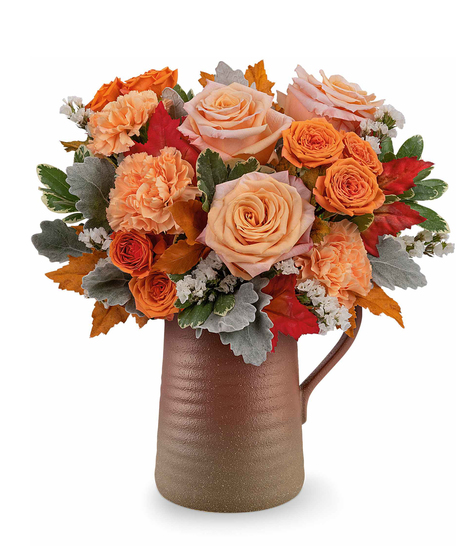 Cider and Clay Bouquet with peach roses, orange spray roses, carnations, and autumn foliage in a rustic Terra Bloom Pitcher.