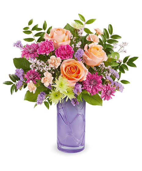 pretty daydream bouquet with peach roses, pink flowers and purple accents in a lavender glass vase