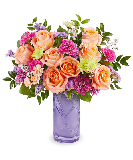 pretty daydream bouquet with peach roses, pink flowers and purple accents in a lavender glass vase
