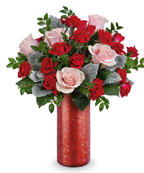 All-around pink and red rose arrangement with dusty miller and huckleberry displayed in a red sparkle glass vase
