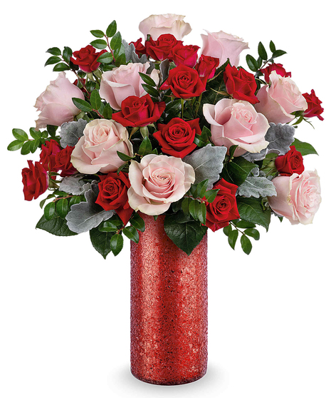 All-around pink and red rose arrangement with dusty miller and huckleberry displayed in a red sparkle glass vase