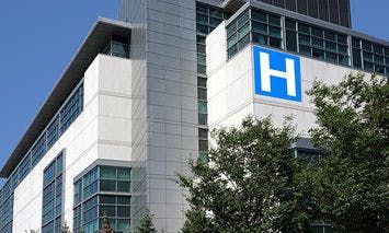 A modern multi-story hospital building, marked with a large blue 